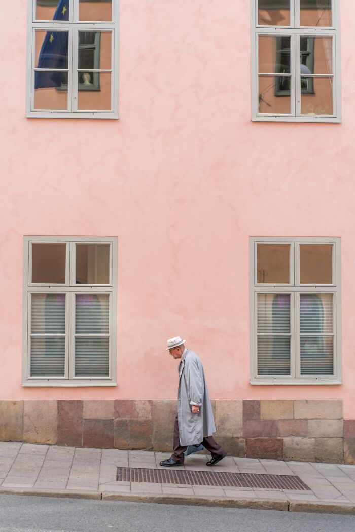 Man in a light coat and hat walks past a pink wall, capturing the essence of Oslo's streets.
