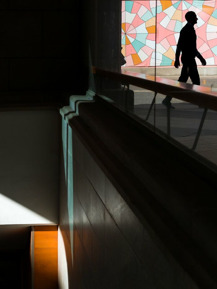 Silhouette of a person walking in Oslo, colorful geometric mural in the background, capturing essence of city's streets.