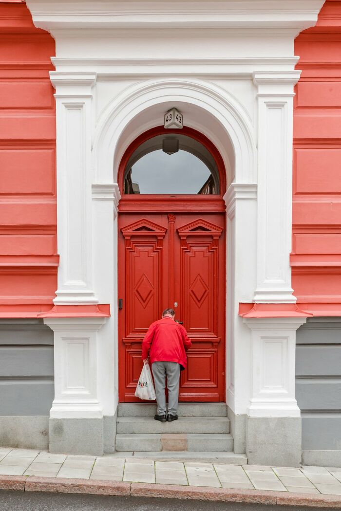 Man in red jacket unlocking a large red door in Oslo street scene.