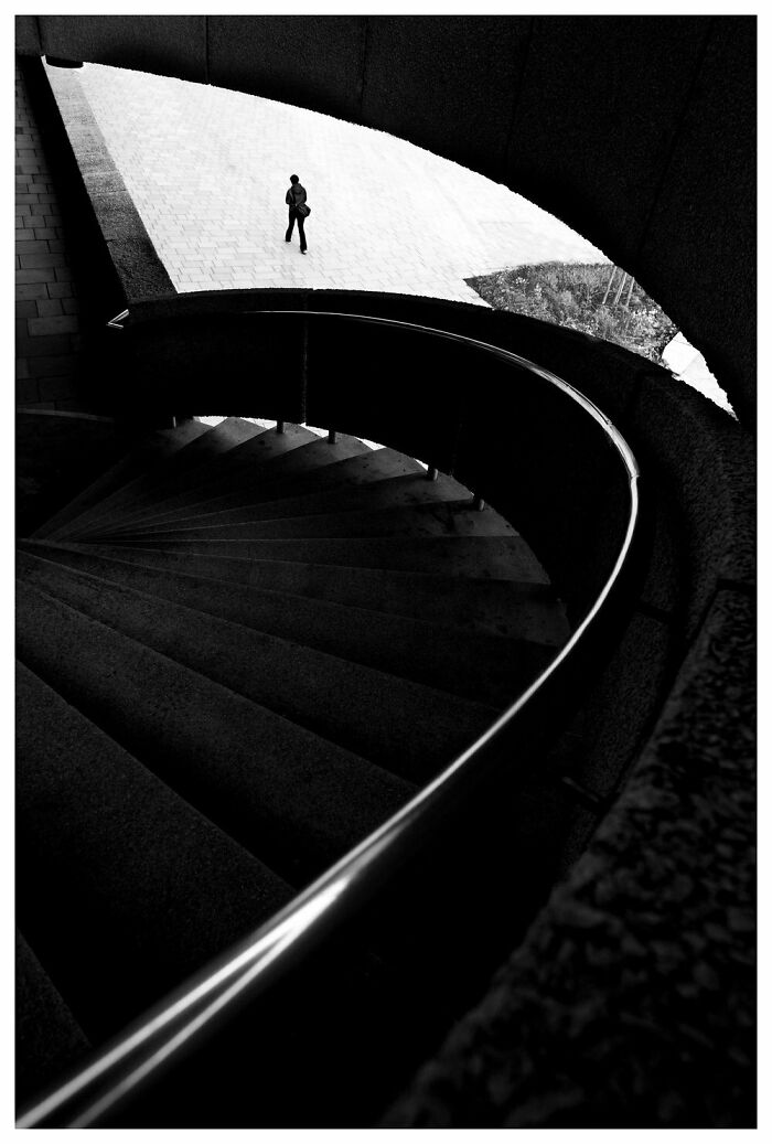 A lone figure walks above a spiral staircase, capturing the essence of Oslo's streets in black and white photography.