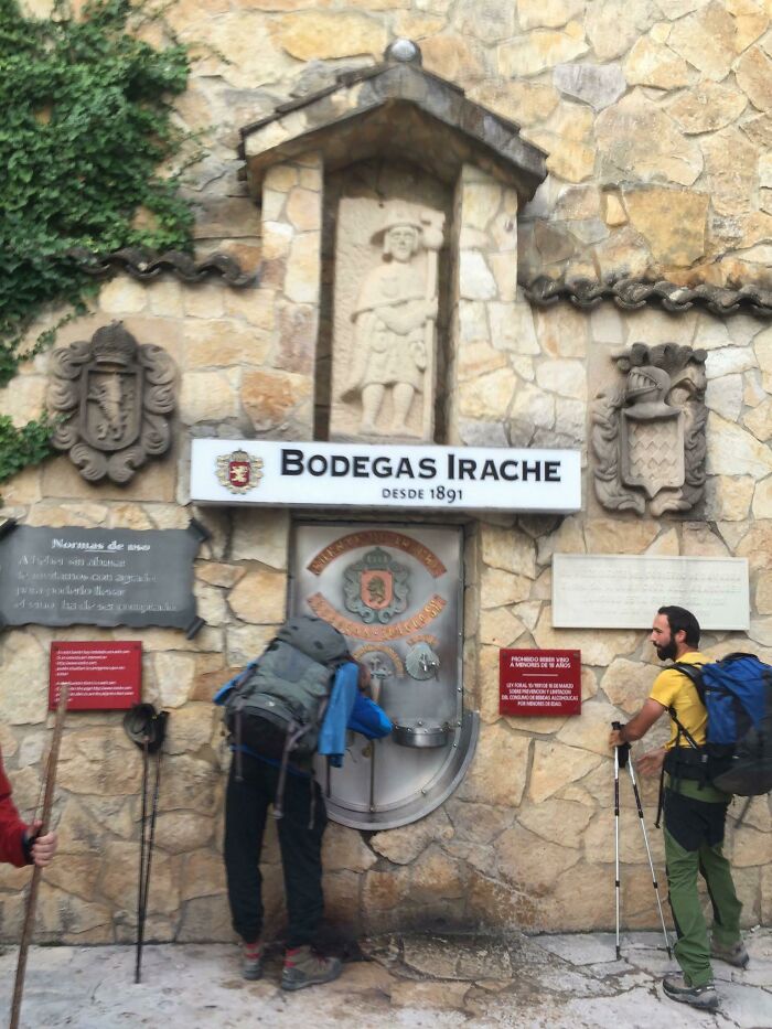Tourists at Bodegas Irache wine fountain, demonstrating interesting experiences on a scenic stone backdrop.