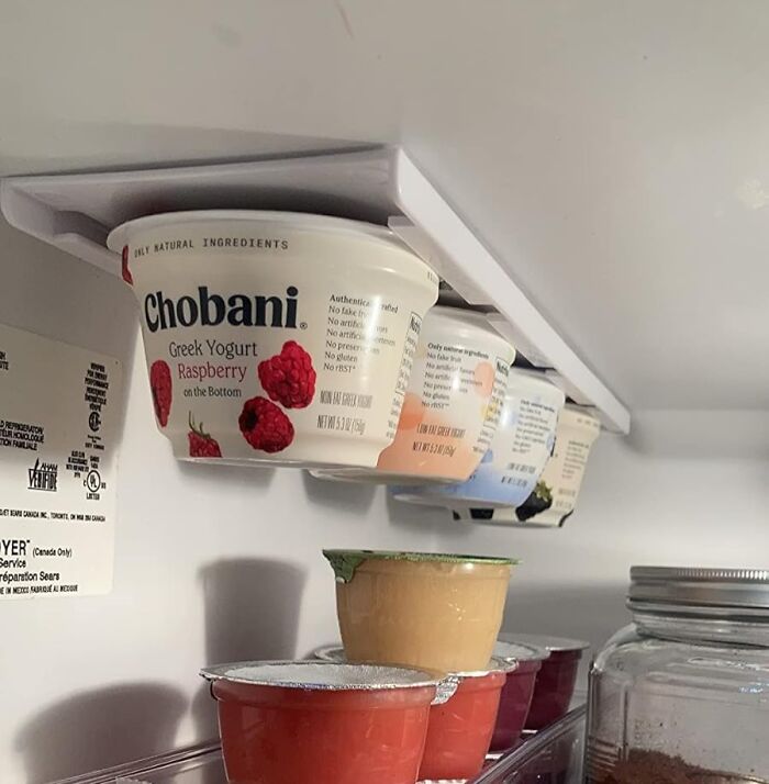 Yogurt cups stored under a shelf using a clever invention, maximizing fridge space and reducing frustration.