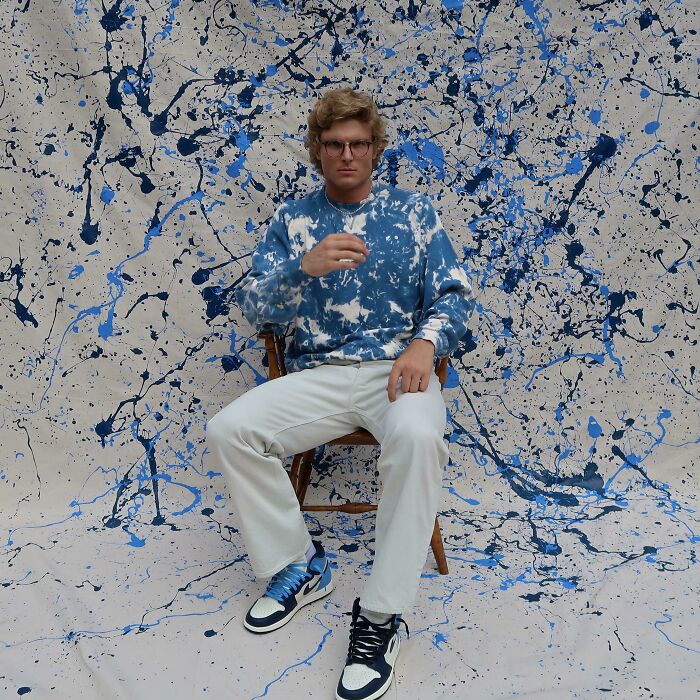 Man wearing splatter-patterned sweater and white pants, embodying bold fashion risks against a matching artistic backdrop.
