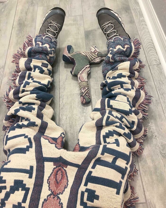 Fashion risks with patterned blanket pants and matching toy on wooden floor.