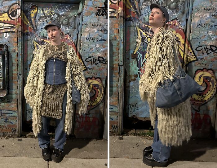 Person posing in eclectic fashion with long shaggy coat, denim corset, and knit dress in graffiti-covered urban setting.