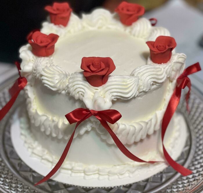 White frosted cake decorated with red icing roses and ribbons, an impressive example of incredible bakes.