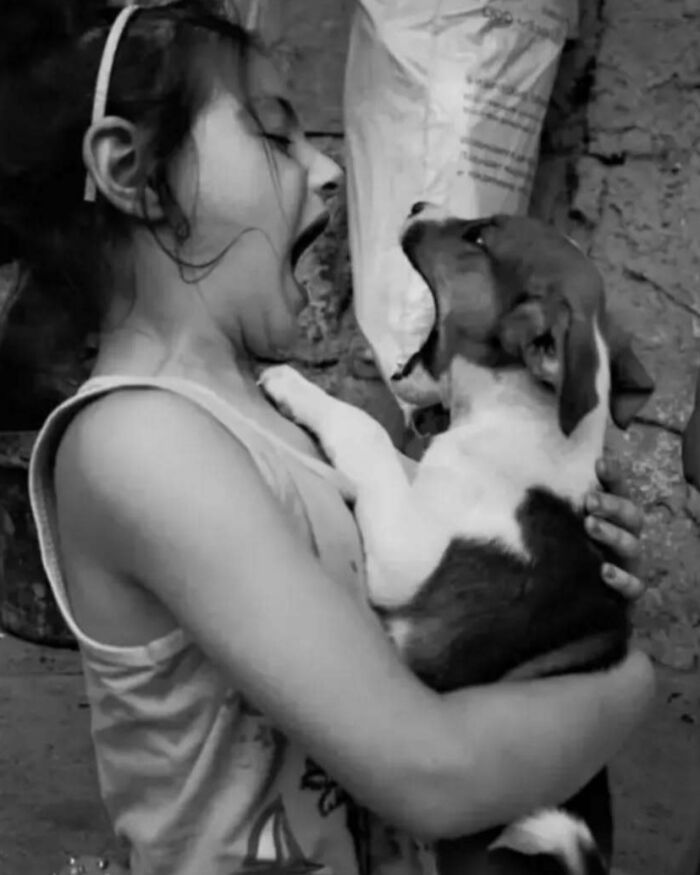 Black and white photo of a child playfully yawning with a puppy, highlighting childhood innocence and resilience.