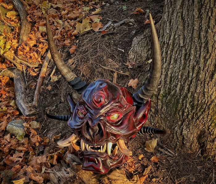 Creepy handmade demon mask with horns, set against an autumn forest floor.