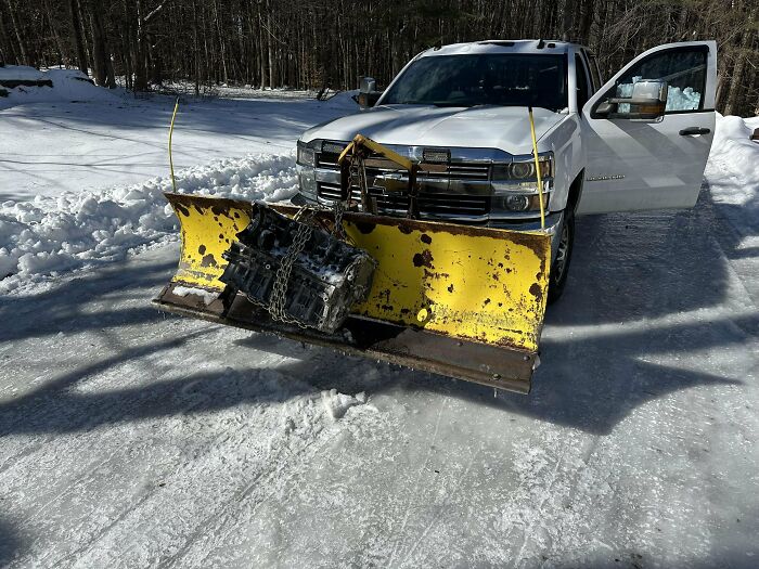 White truck with a rusted yellow snowplow attachment featuring an improvised redneck engineering modification on icy road.