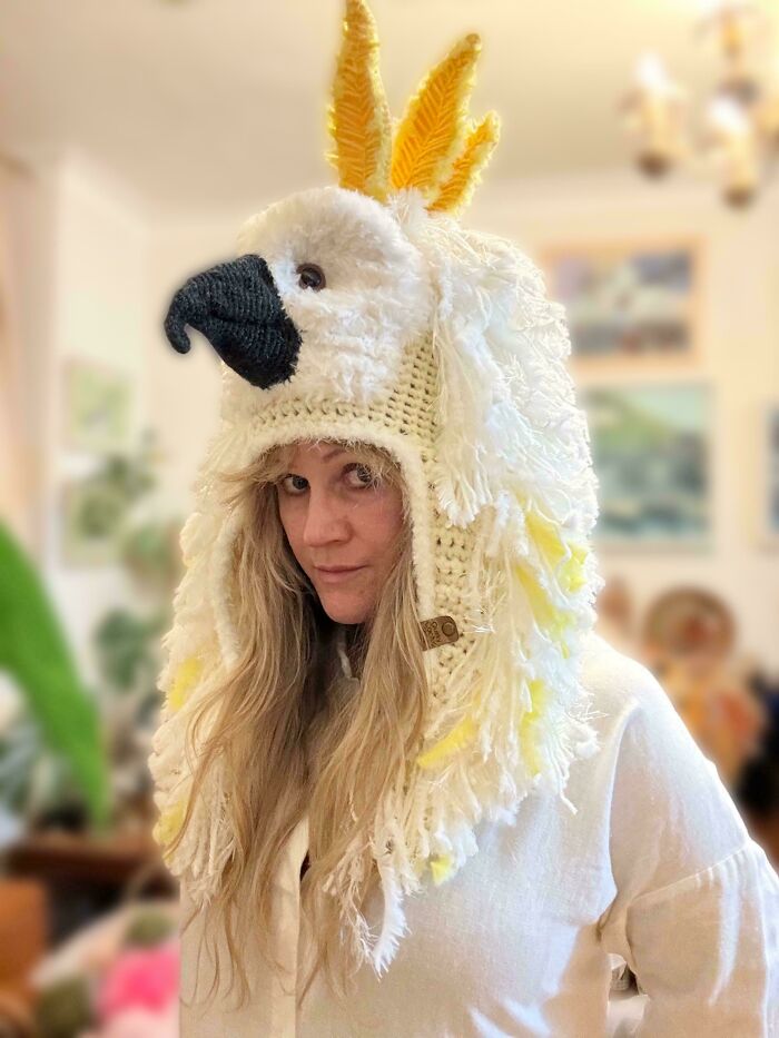Person wearing a DIY crocheted bird hat with yellow feathers indoors.