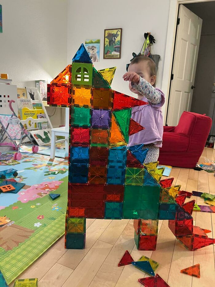 Child playing with colorful magnetic tiles dinosaur structure in a living room, showcasing wholesome dads parenting moments.