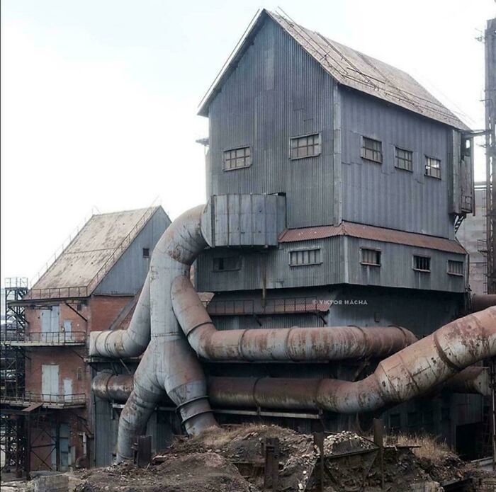 Industrial building with large rusted pipes and dark metal walls, emitting an evil aura like a supervillain headquarters.