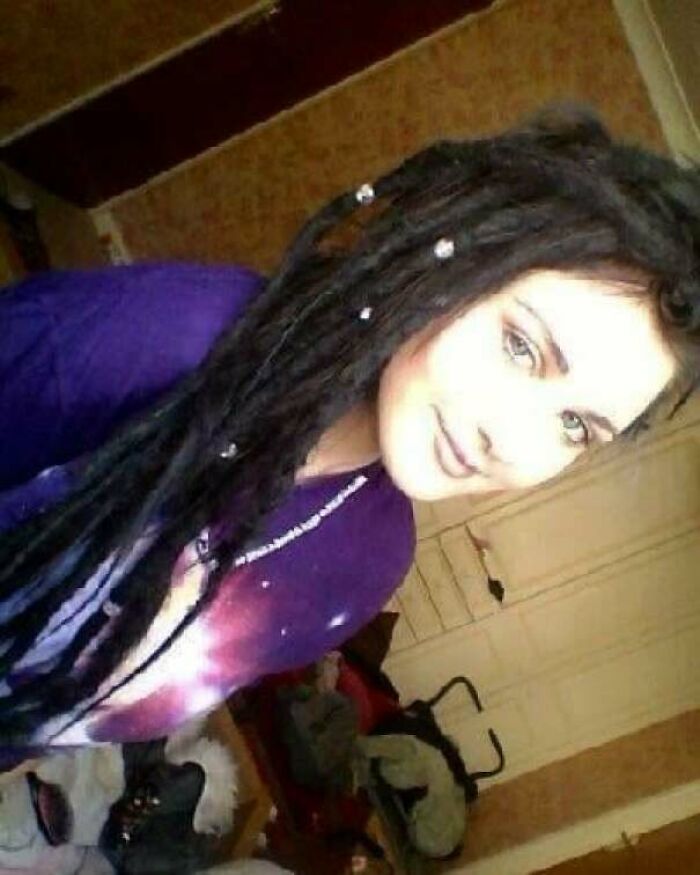 Young woman with long dreadlocks wearing a purple shirt in a messy room, part of regrettable past cringe pics collection.