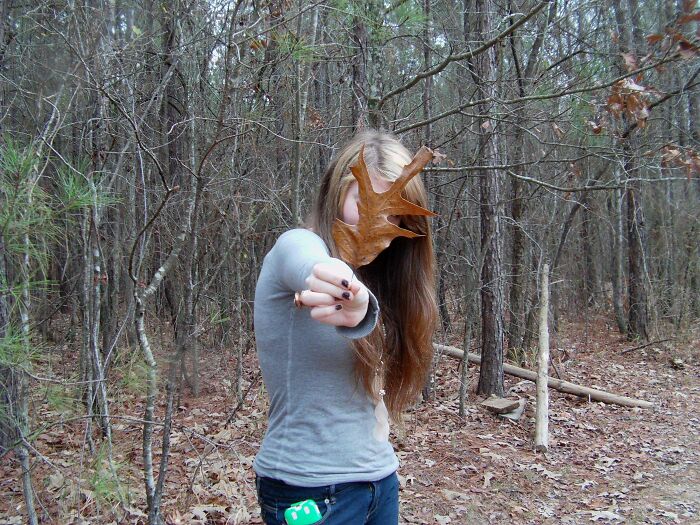 Person holding a large leaf covering their face in a forest, one of many regrettable past pics causing cringe moments.