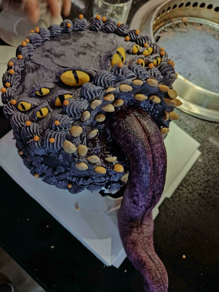 Dark purple monster-themed cake with detailed eyes, decorative frosting, and a long textured tongue, one of the incredible bakes.