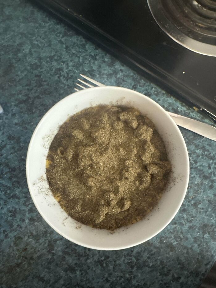 Bowl of macaroni noodles covered in excessive black pepper sitting on a kitchen counter showing a stupid dish.