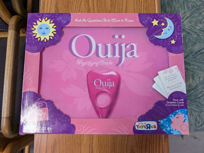 Pink Ouija board game with question cards, a thrift store find displayed on a wooden surface.