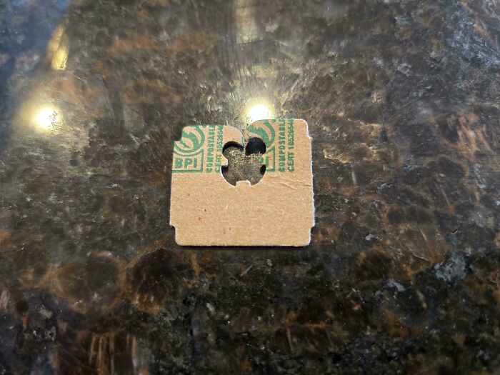 Small torn cardboard piece with a fruit clip hole, highlighting consumerism waste on a dark marble surface.