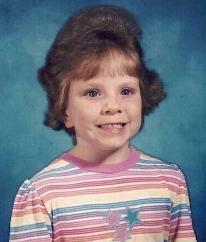 Child with high teased hair, wearing a colorful striped shirt; representing 1980s and 1990s hair disasters.