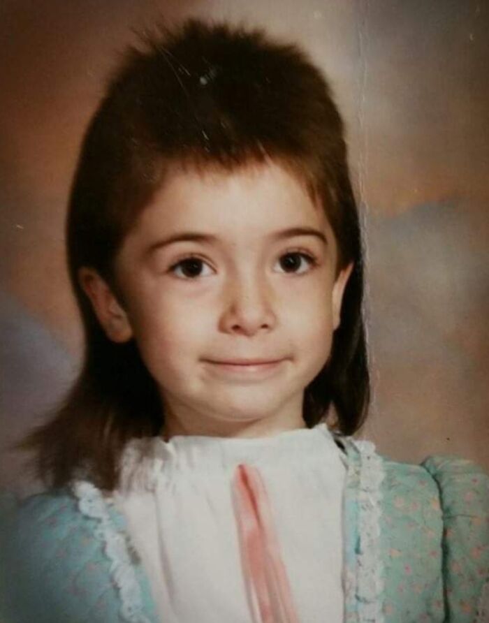 Child with unique 1980s hairstyle wearing a vintage dress, showcasing an epic hair disaster from the era.