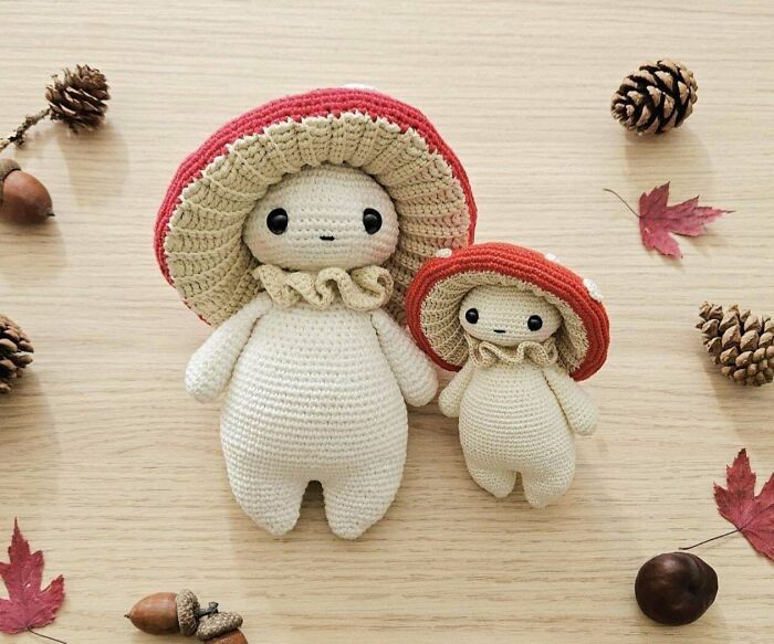 Two adorable crochet masterpieces resembling mushrooms, surrounded by pinecones, acorns, and autumn leaves on a wooden surface.