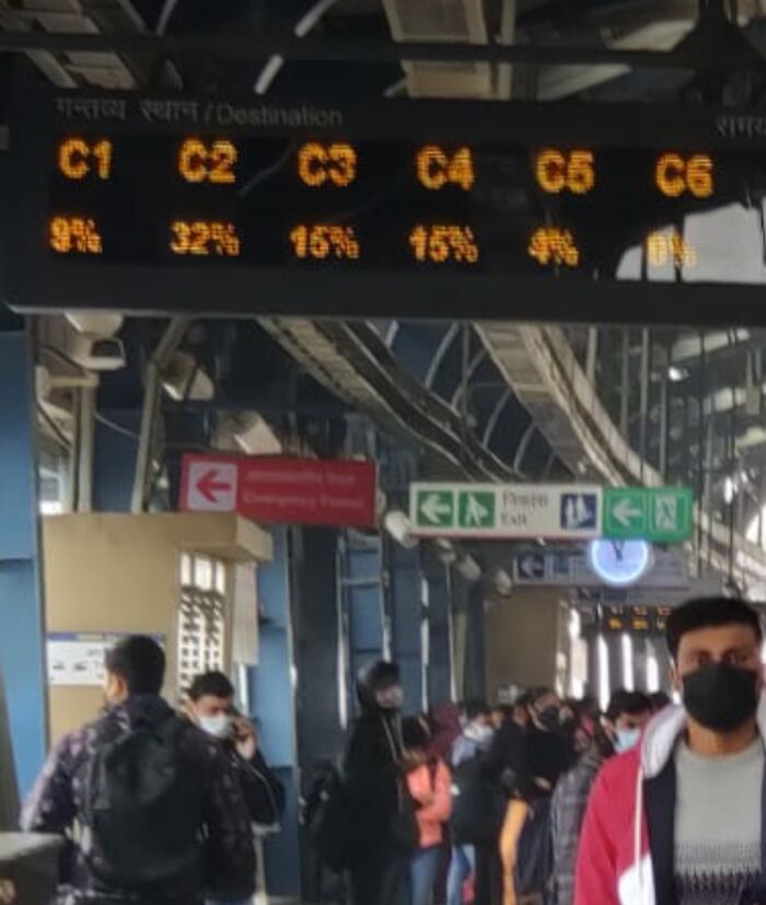 Train station platform with LED display and masked travelers, offering tourist interesting experiences.