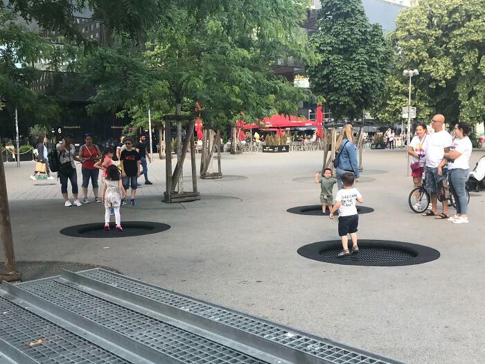Children playing on grates in a lively park setting, capturing unique tourist experiences.