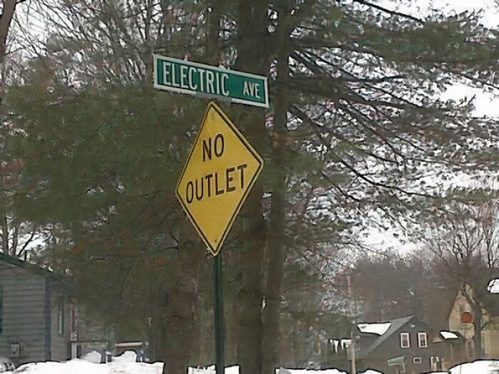 Electric Avenue sign with a "No Outlet" warning, blending humor and positivity in a snowy rural scene.