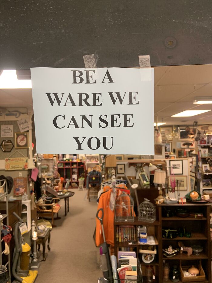 Sign with misspelling, reads “BE A WARE WE CAN SEE YOU” in a cluttered shop, making grammar police cringe.