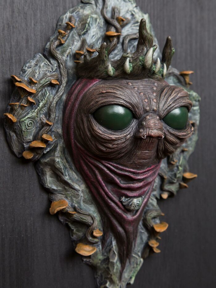Creepy handmade craft of an alien-like face with large eyes and a crown, surrounded by fungi and leaves.