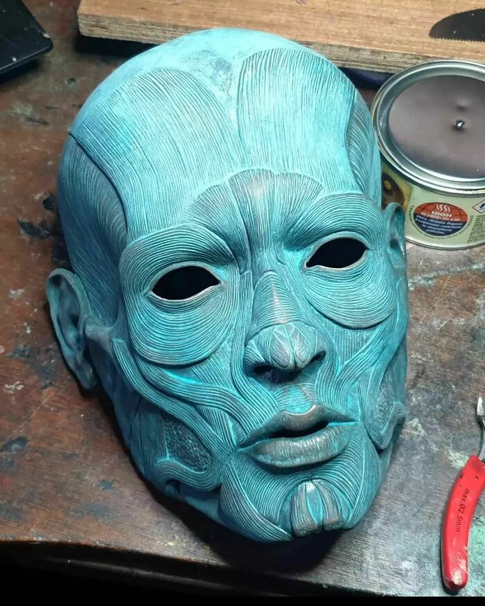 Creepy handmade mask with detailed facial muscle design, placed on a workshop table with tools.