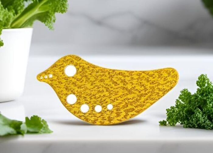 Yellow bird-shaped herb s******r tool on a kitchen counter surrounded by fresh greens, showcasing clever inventions for kitchen use.