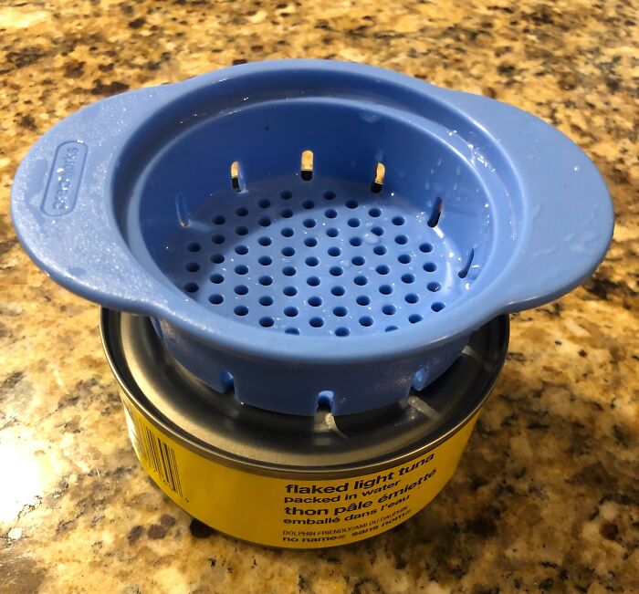 Innovative tuna can strainer minimizes frustration, sitting atop a can on a kitchen counter.