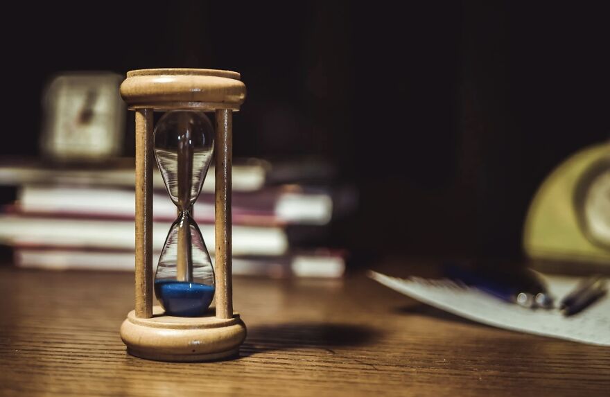 Hourglass with blue sand on a wooden table, symbolizing ethical dilemmas and the passage of time.