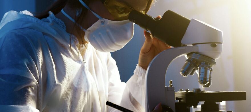 Scientist in protective gear using a microscope, illustrating ethical dilemmas in scientific research.