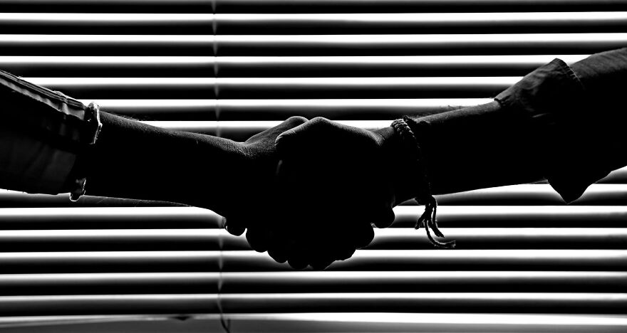 Silhouetted handshake in front of window blinds representing ethical dilemmas and decision-making.