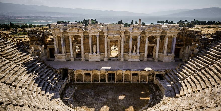 Ancient amphitheater with stone seating and a grand stage, potentially sparking ethical dilemmas in historical contexts.