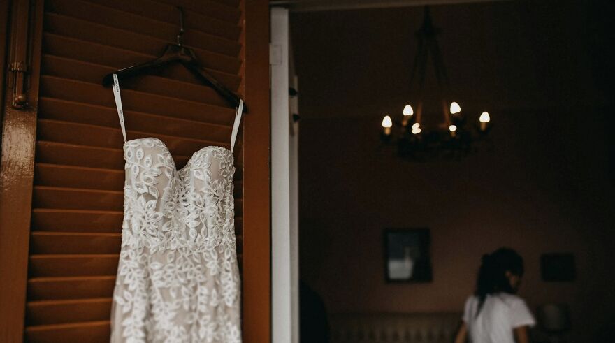 Lace wedding dress hanging; person in dimly lit room. Ethical dilemmas concept.