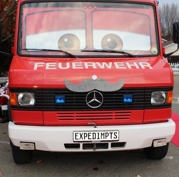 Funny fire truck with mustache decoration, resembling Archie McPhee items, parked on a street.