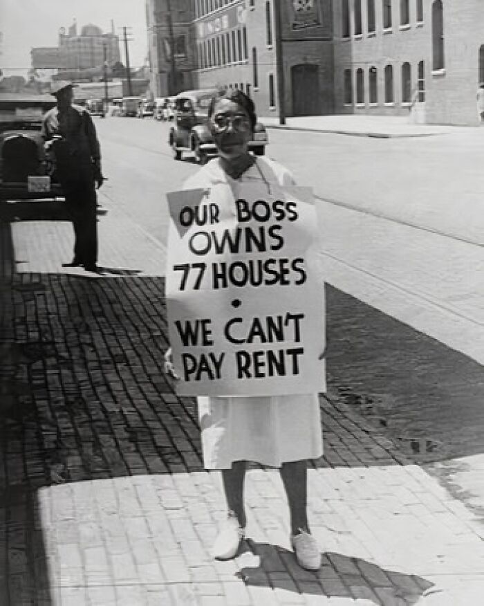Protester holding anti-capitalism sign on urban street, highlighting housing inequality issues.