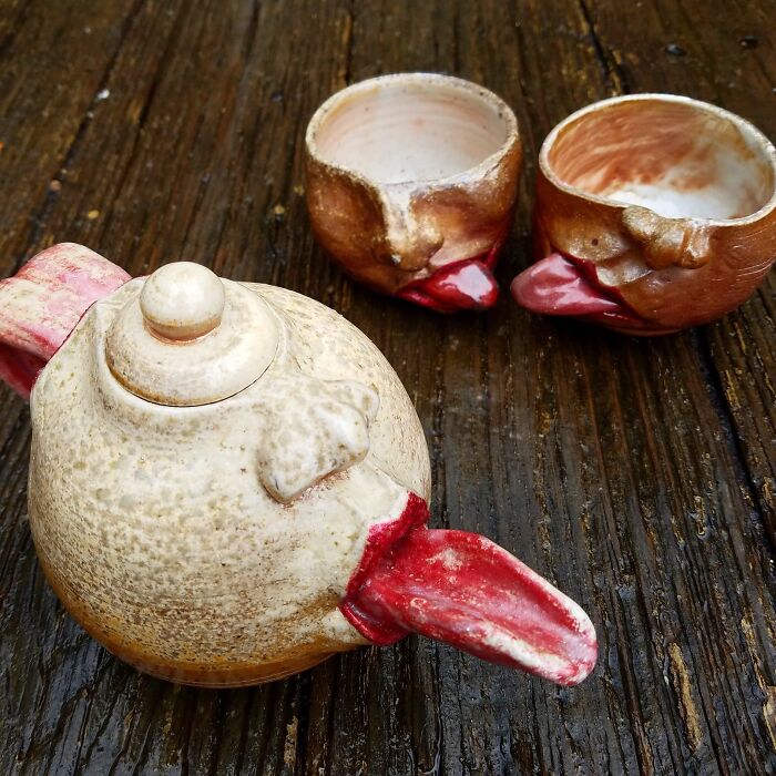 Creepy handmade teapot and cups with red beaks on a wooden surface.