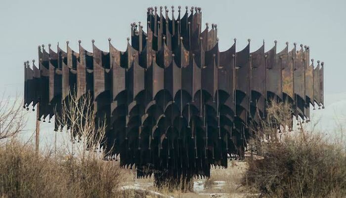 Abstract dark metal structure in a barren landscape, resembling a building with an evil aura like a supervillain headquarters.
