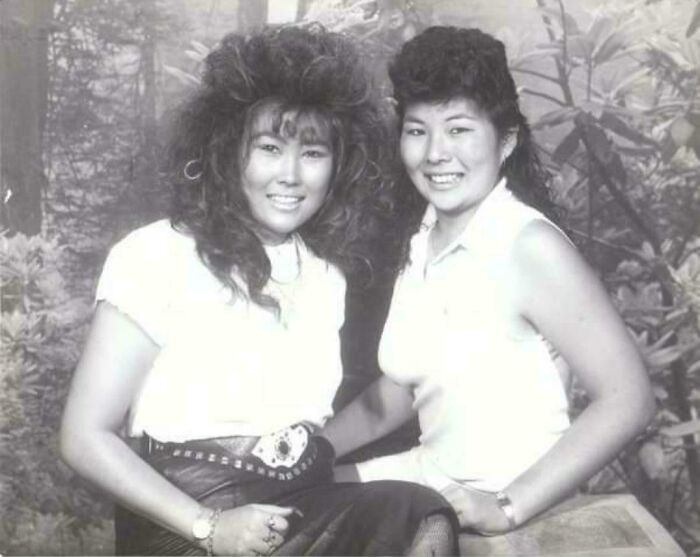 Two women with big 1980s hair, smiling in a vintage photo studio setting.