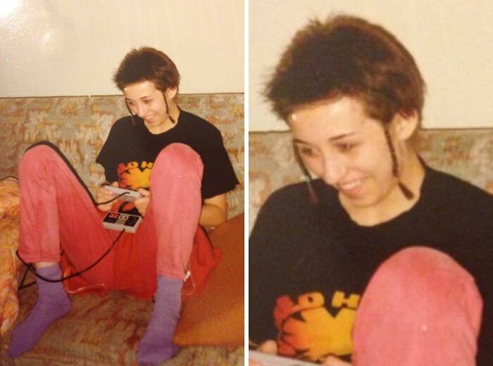 Person with an epic 1980s hair disaster, sitting on a couch, playing a video game console, wearing colorful pants and socks.