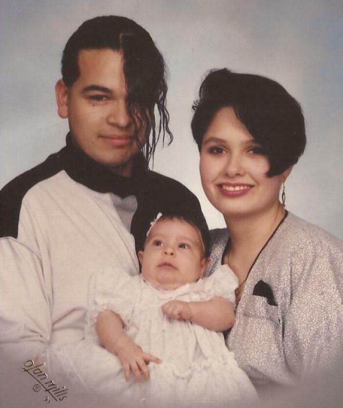 80s and 90s family photo with unique hairstyles; man with side-swept bangs, woman with short hair, holding a baby.