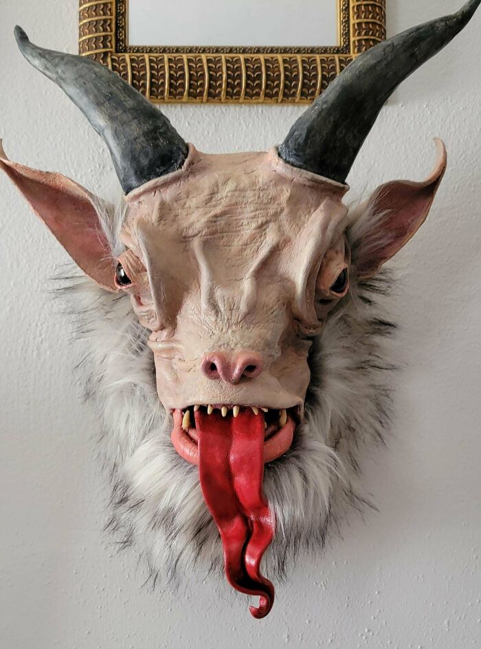 Creepy handmade craft of a horned creature with a long red tongue and fur, mounted on a wall.