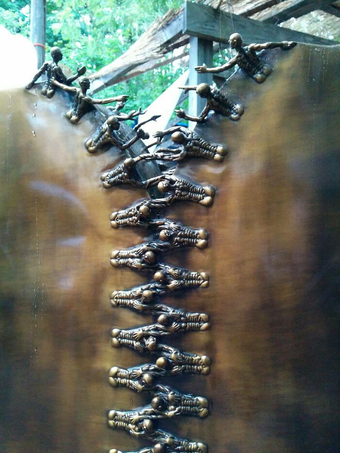 Creepy handmade crafts: bronze skeleton figures forming a zipper, outdoor setting.