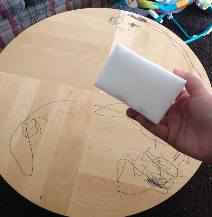 Hand holding a cleaning sponge over a wooden table with crayon marks, preparing for spring cleaning headstart.