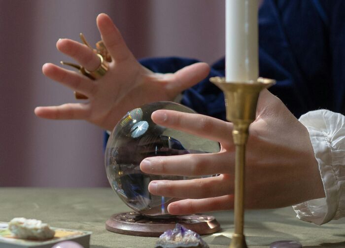 Hands hovering over a crystal ball surrounded by candles, representing weird government projects.