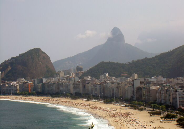Retro Brazilian beach scene with waves, bustling shore, and iconic mountains in the background.